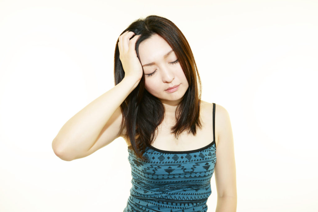 目を閉じてこめかみを押さえる女性