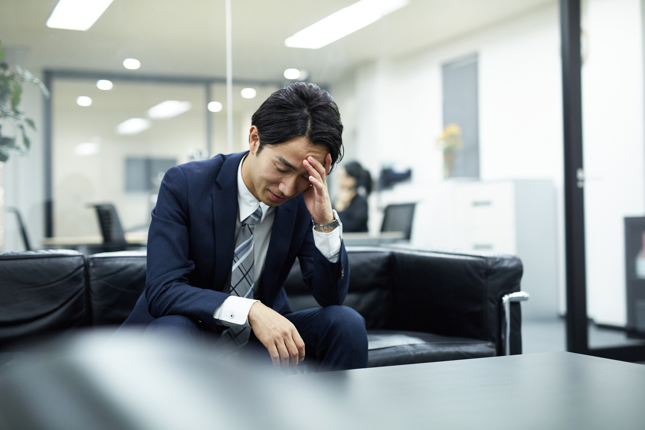 オフィスで額を押さえて座り込む男性