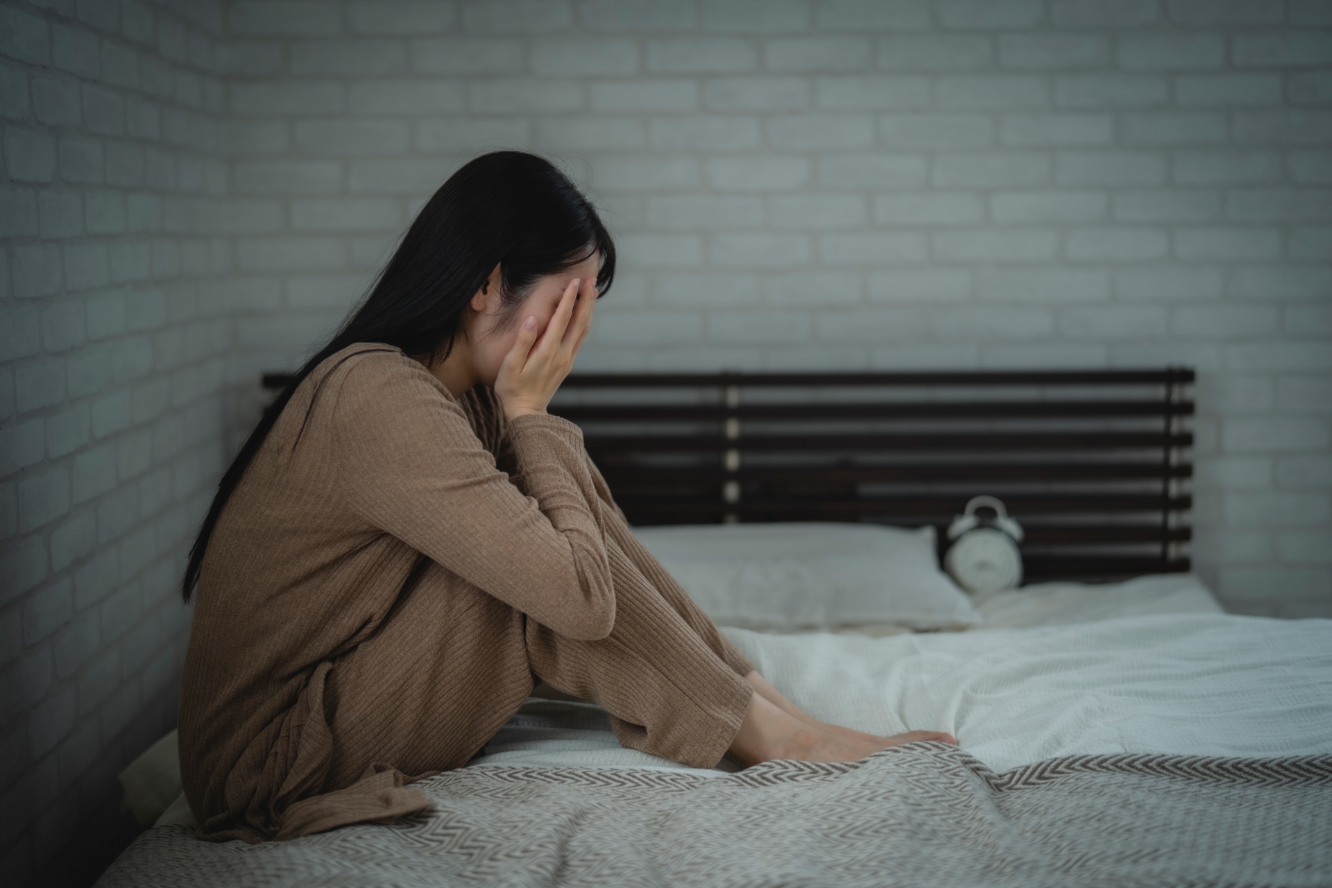 眠れずにベッドの上でしゃがみこむ女性